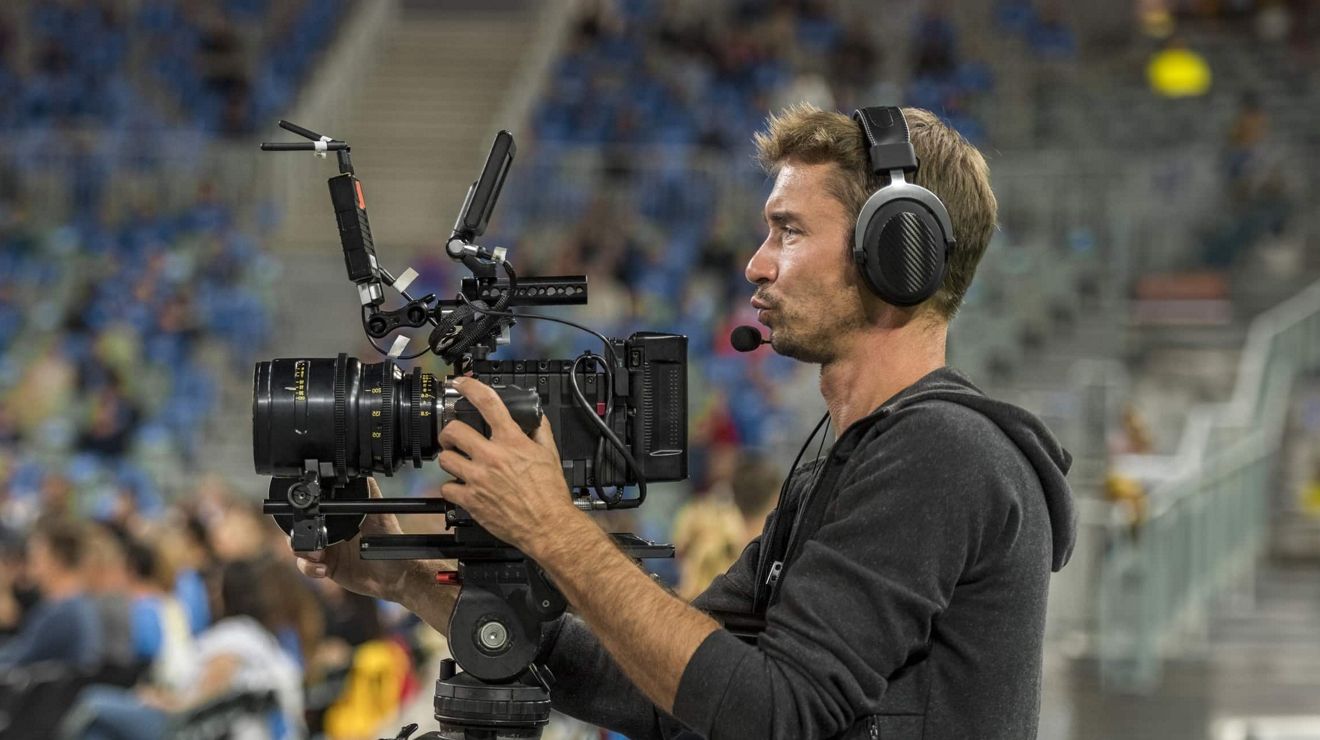 A person operates a professional-grade camera from the floor of an arena.