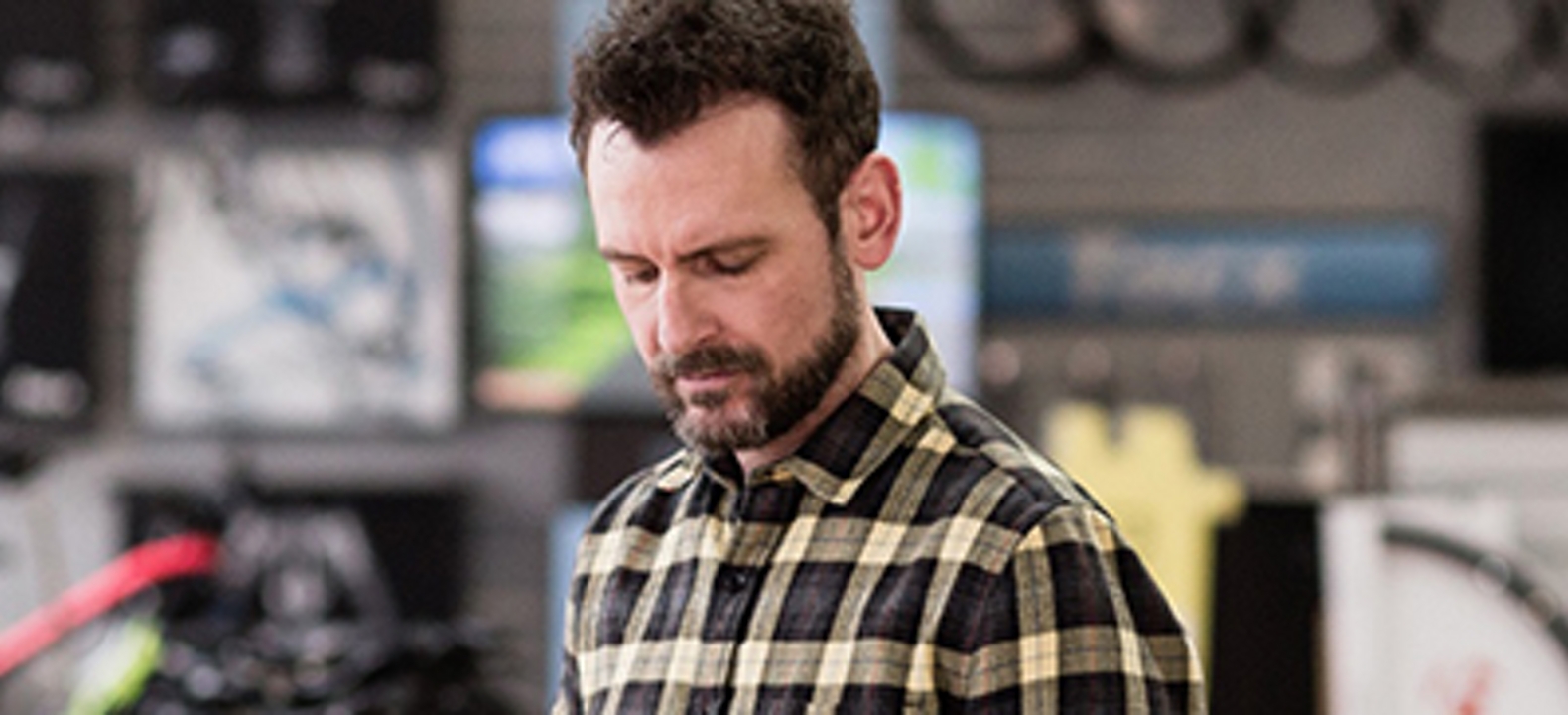 White man in plaid shirt looking down at tablet 