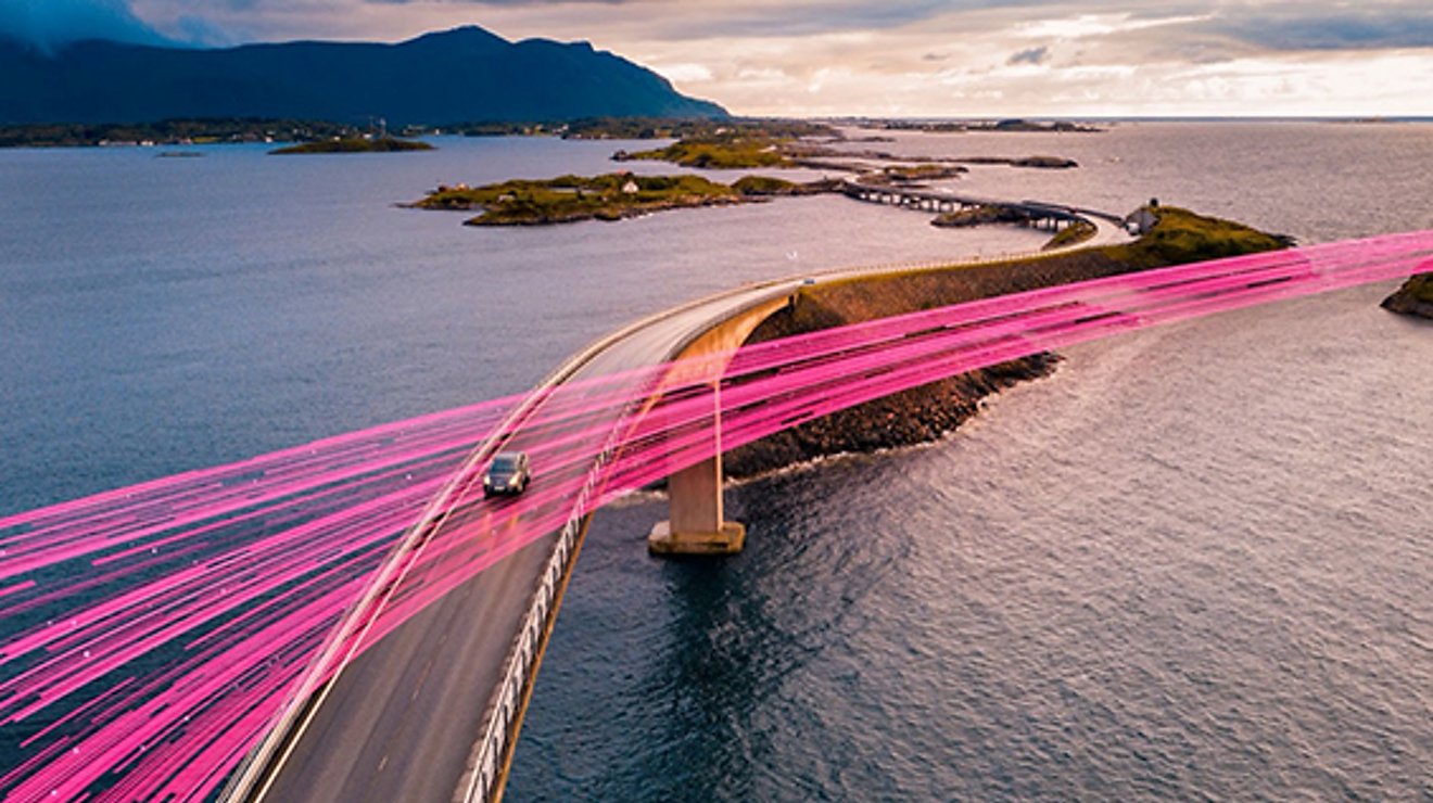 A single car drives on an ocean highway. Magenta beams indicate connectivity even in rural areas.
