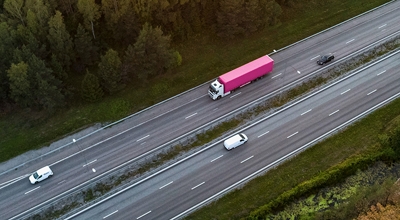 Arial view of a semi-truck hauling a magenta trailer and traveling down a highway