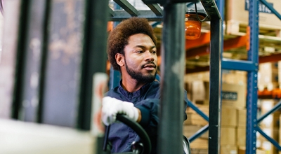 Closeup of a man driving a forklift through a warehouse