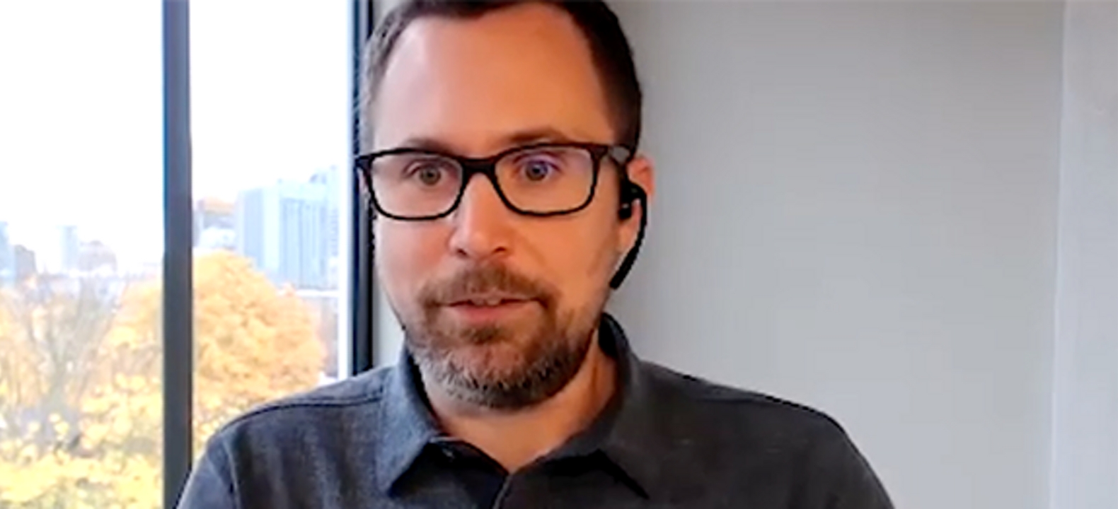 Closeup of man with beard, mustache, glasses and black button down shirt with a window to his side