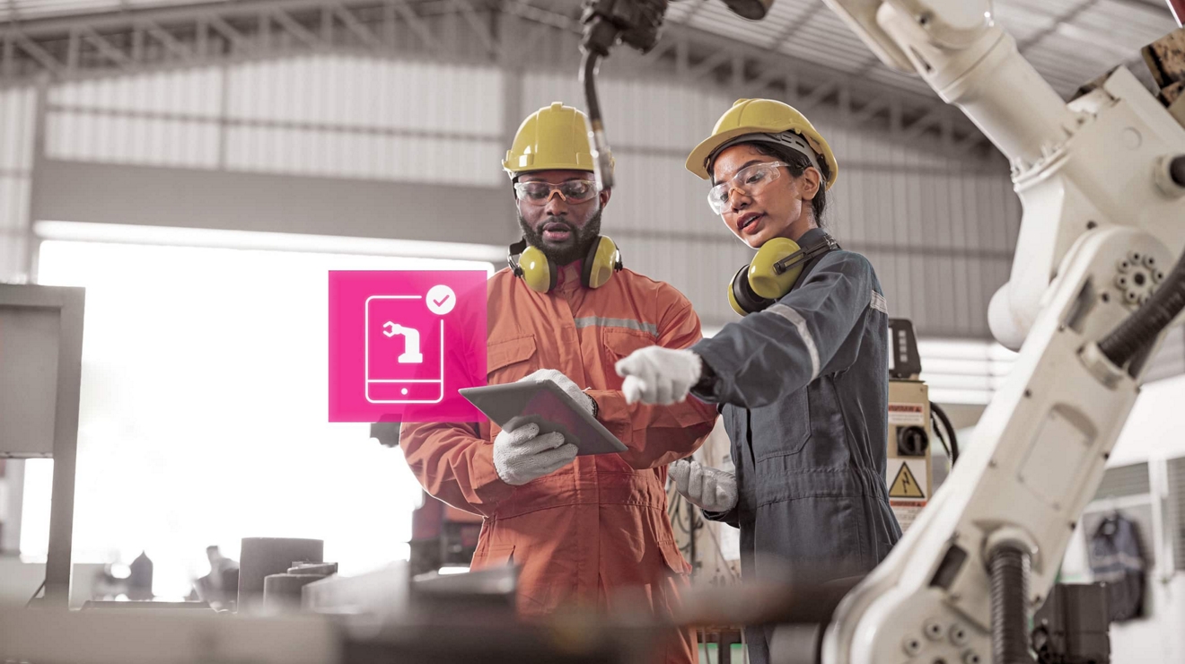 Manufacturing plant workers hold a digital tablet and discuss an alert about an assembly line robot.