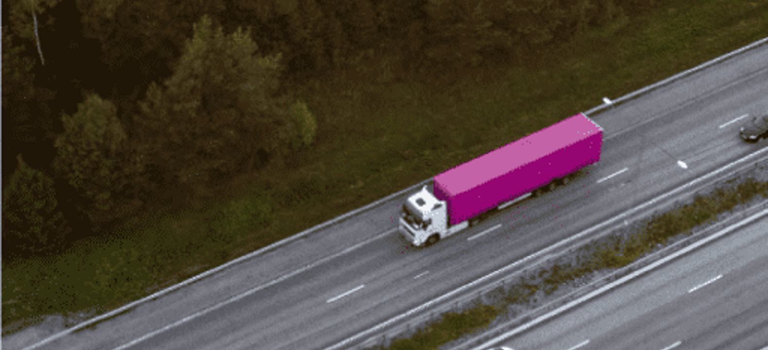 Magenta semi-truck travels on a highway.