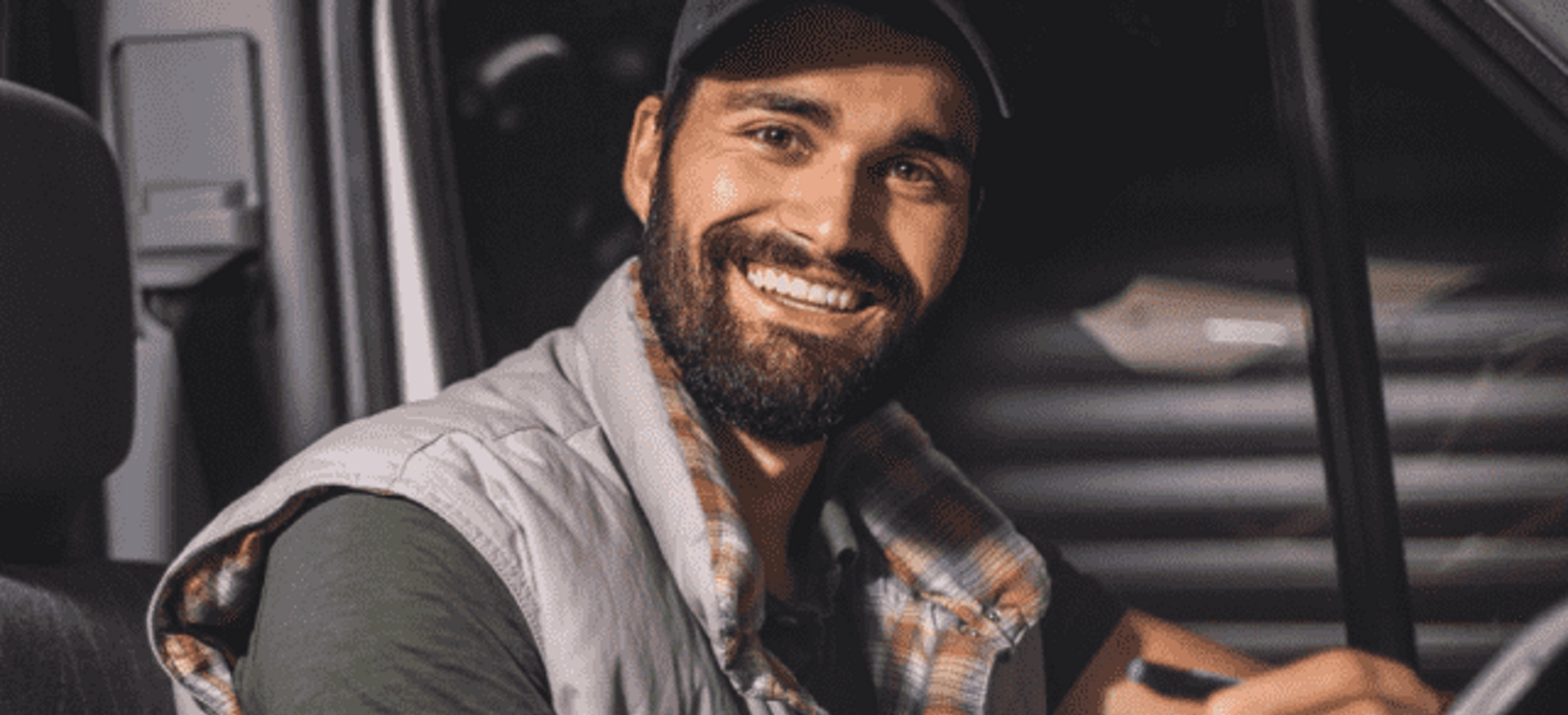 Driver smiles at the camera while completing paperwork in the driver’s seat of his vehicle. 