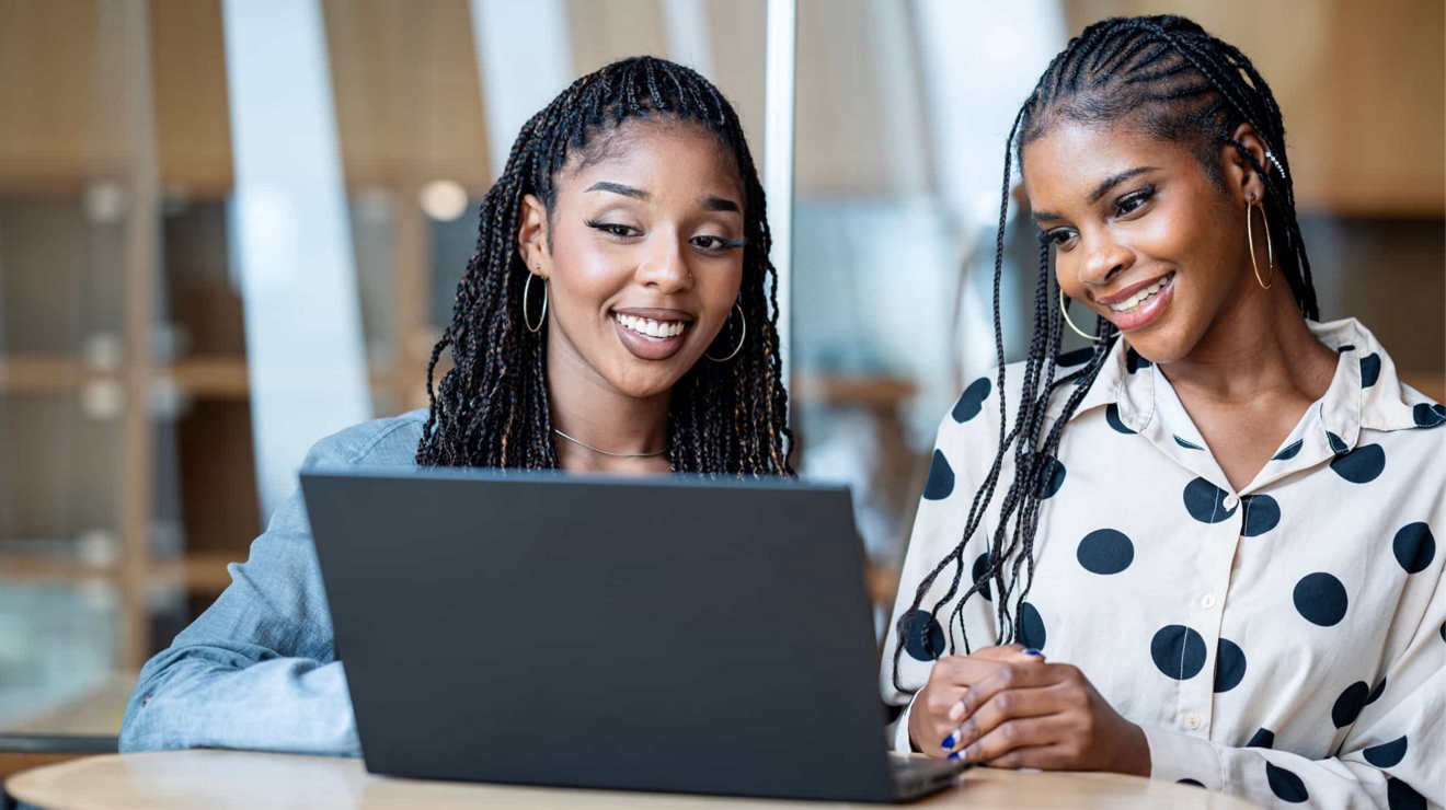 Two smiling business professionals share a laptop to attend an online meeting.