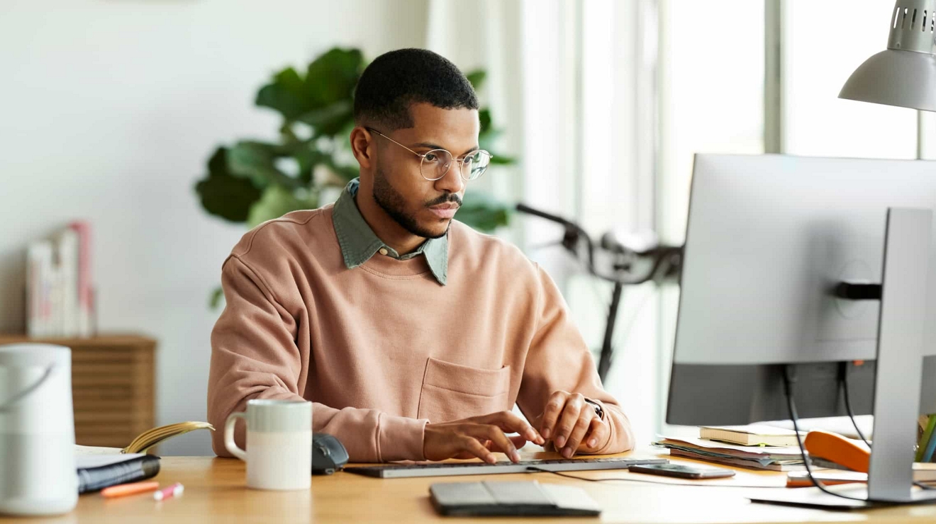 A business professional at a desk in their home office, working on their laptop and mobile phone.