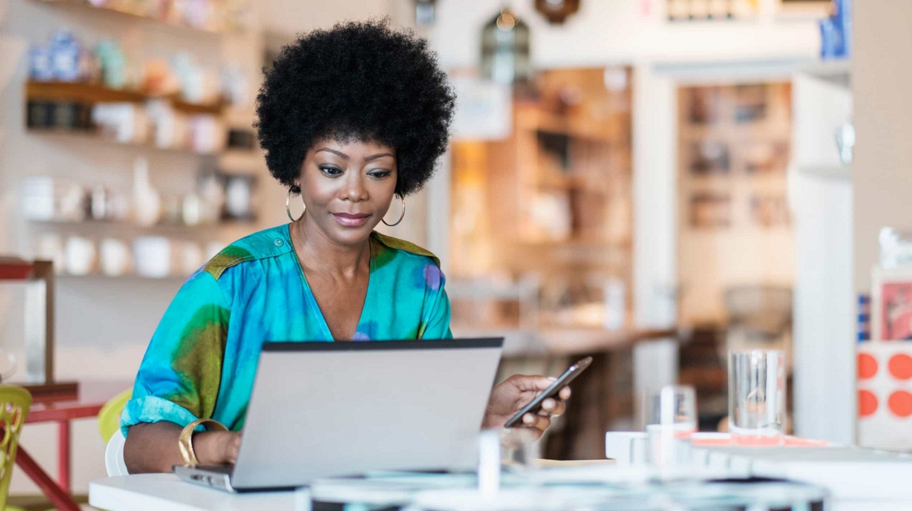A business professional at a desk in their home office, working on their laptop and mobile phone.