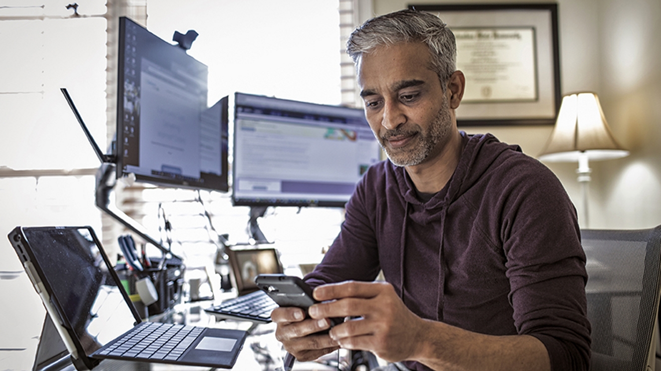 A government employee works from home on a connected laptop and their smartphone.