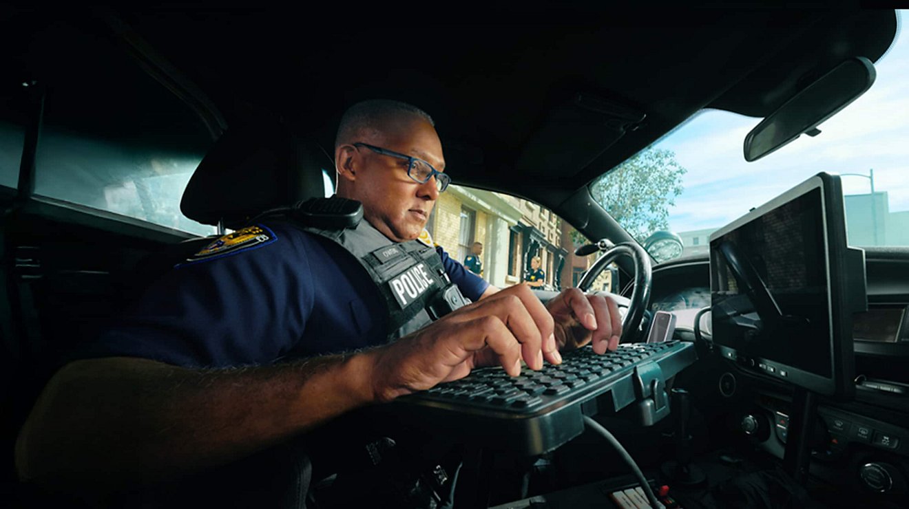 A police officer inside a connected patrol car uses a monitor and keyboard to transmit updates.