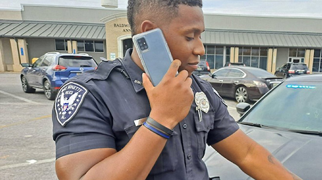 Police officer on his smart phone standing near vehicles in a commercial parking lot