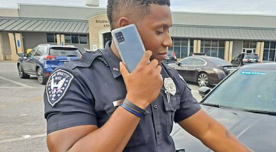 Police officer on his smart phone standing near vehicles in a commercial parking lot