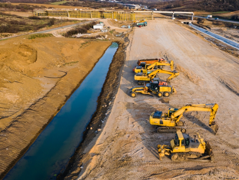 Overhead view of several yellow earth-moving equipment vehicles on sand.