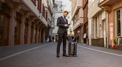 A financial service professional with a suitcase checks his smartphone in the middle of a pedestrian street.