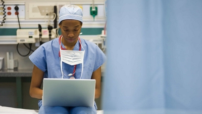 A surgeon in a hospital treating room enters patient data into a laptop.