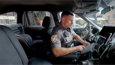 A police officer in a car sends data via high-speed wireless using a smartphone and external keyboard.