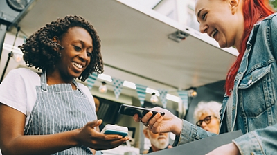 Store worker in apron uses mobile device to let customer pay with her smartphone