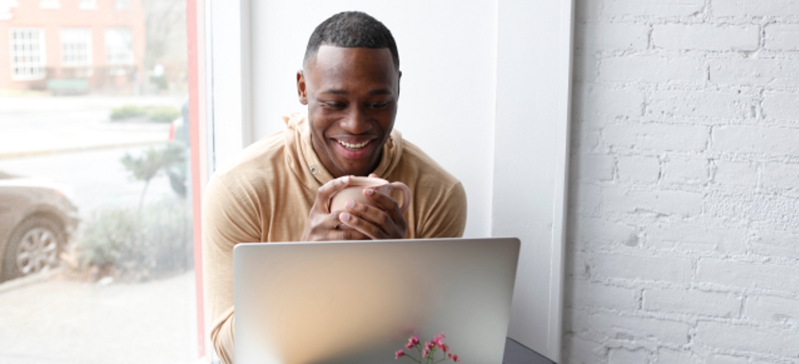 A smiling professional takes a meeting on his laptop in a coffee shop.