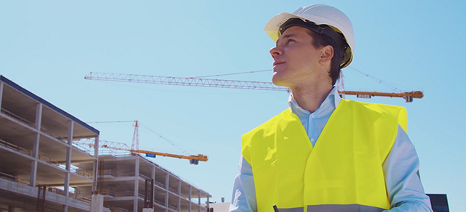 Man in factory setting with hardhat and vest looks down at a tablet.