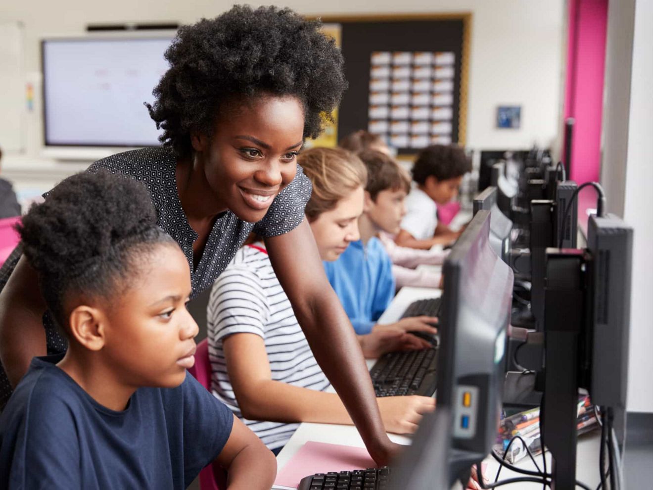 Teacher and student looking at computer in a busy classroom.