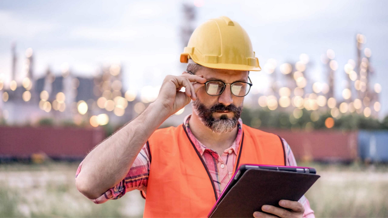 An oil refinery worker securely checks their tablet while standing outside the plant.