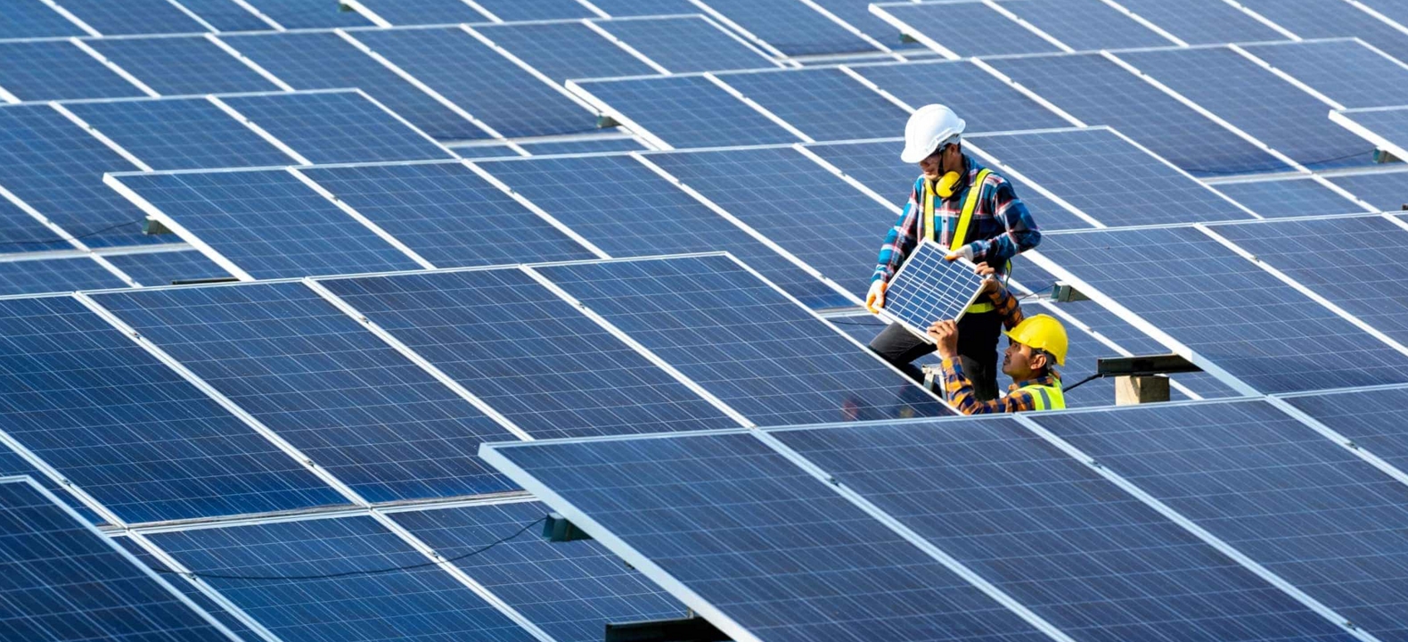 A worker replaces a solar panel in a solar farm while a crew member assists.