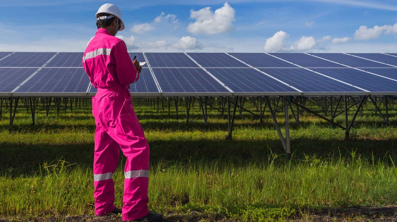 An energy technician writes on their tablet while examining panels at a solar panel facility.
