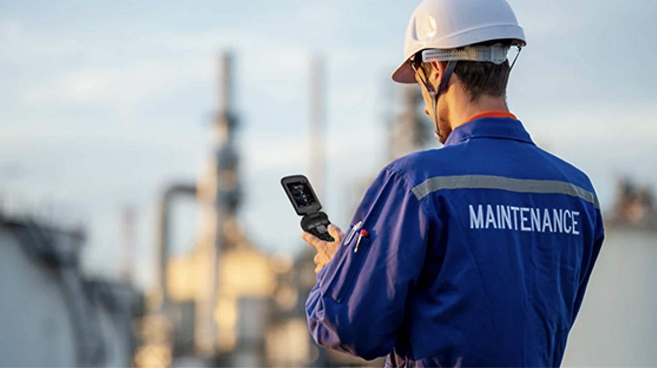 A maintenance worker standing in front of an oil refinery checks their mobile device.