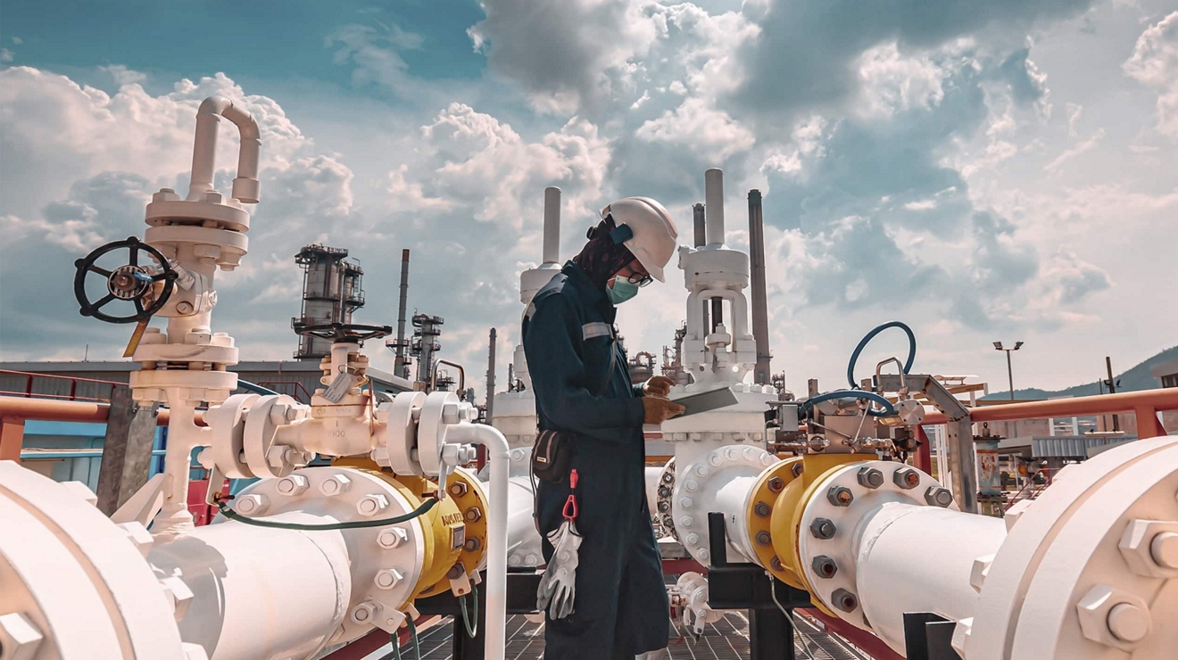 An inspector checks a steel oil pipe and looks up information on their tablet.
