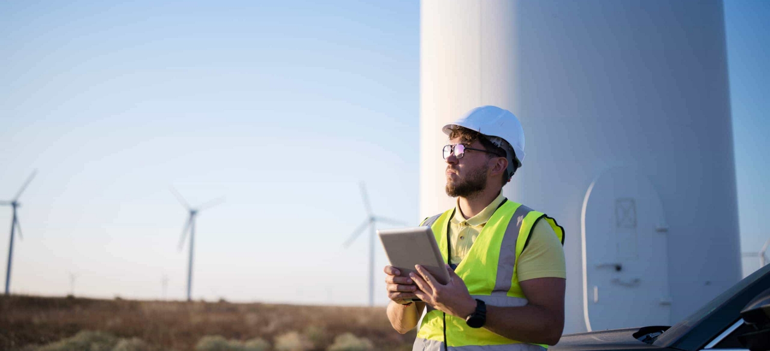 A utilities worker at a wind farm surveys the horizon with their 5G-connected device in hand.