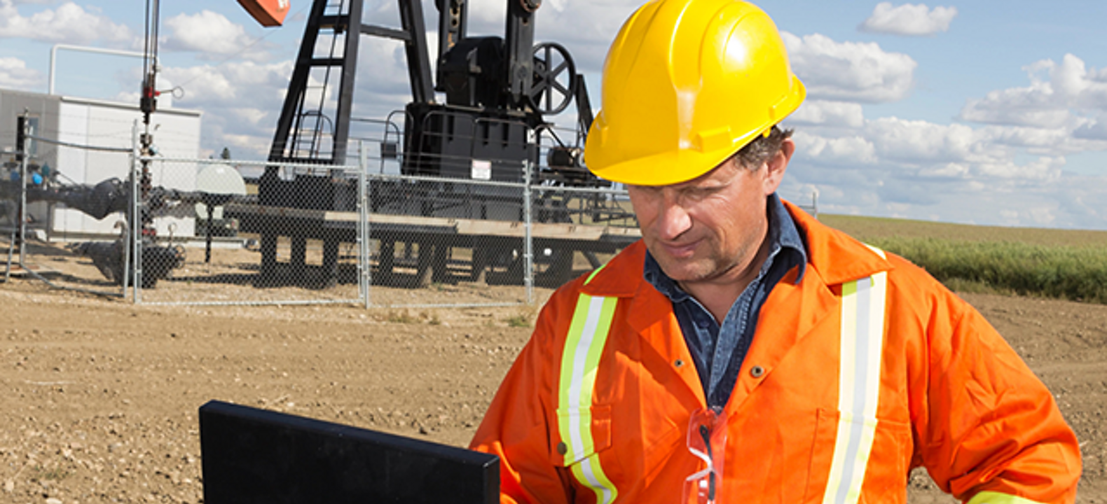 An oil worker checks his laptop at a pumpjack site.