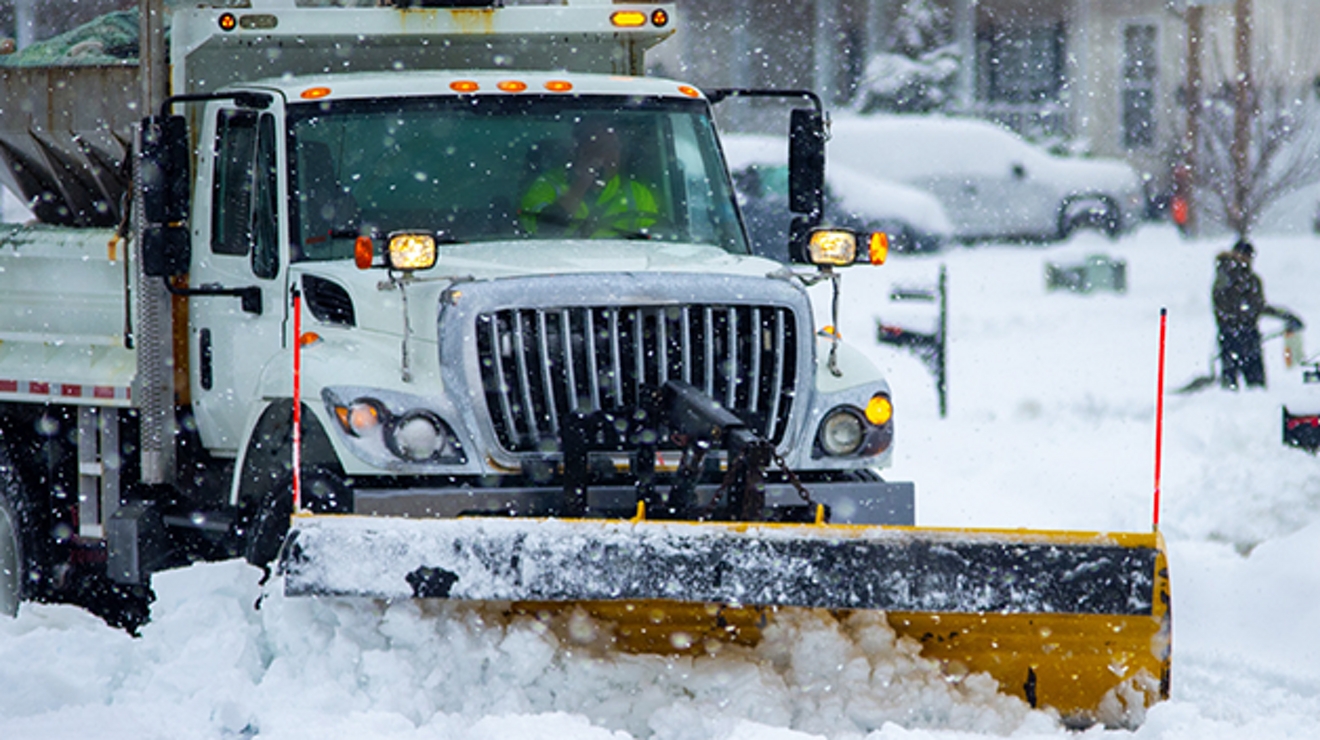 A large dump truck with a snowplow clears public streets after a heavy snowfall.