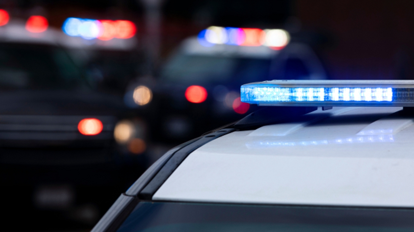 A police cruiser flashes blue lights, and in the background, two more cruisers flash red and blue lights.