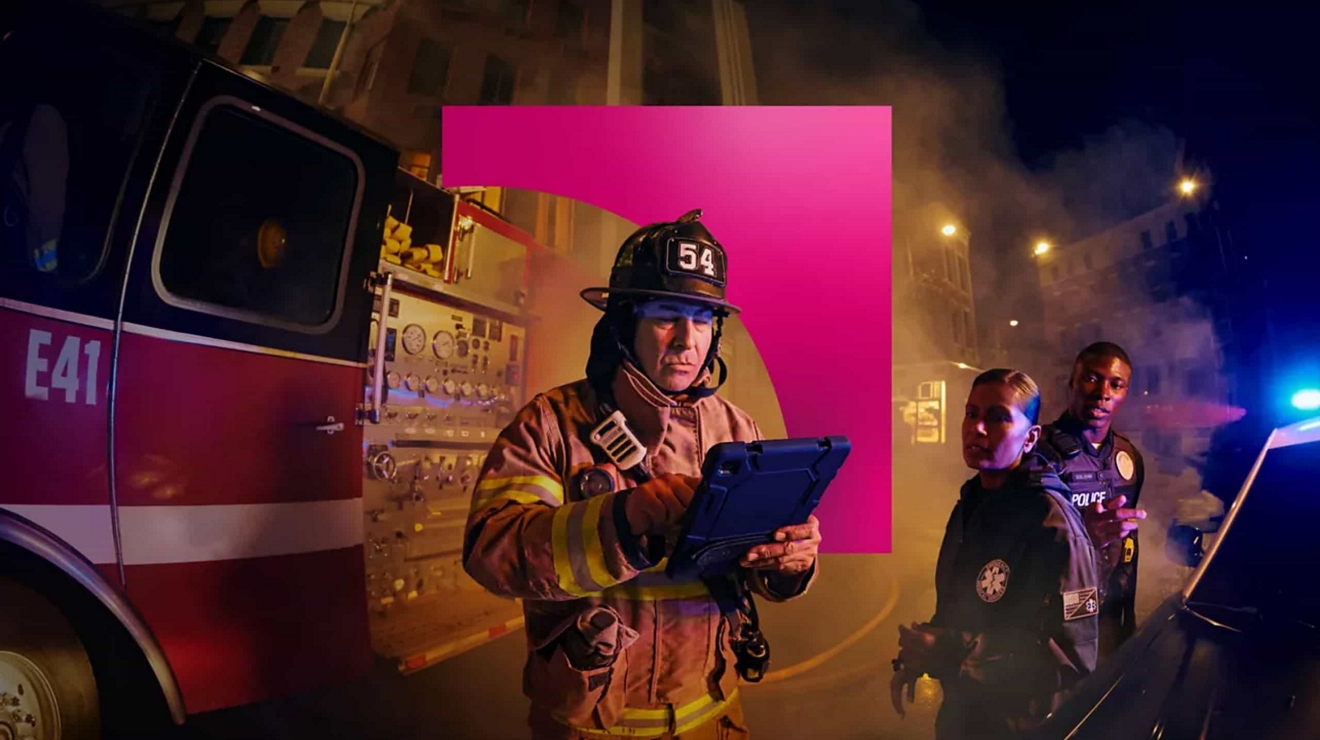 A firefighter enters data on a mobile device near a fire engine at a night fire in an apartment block.