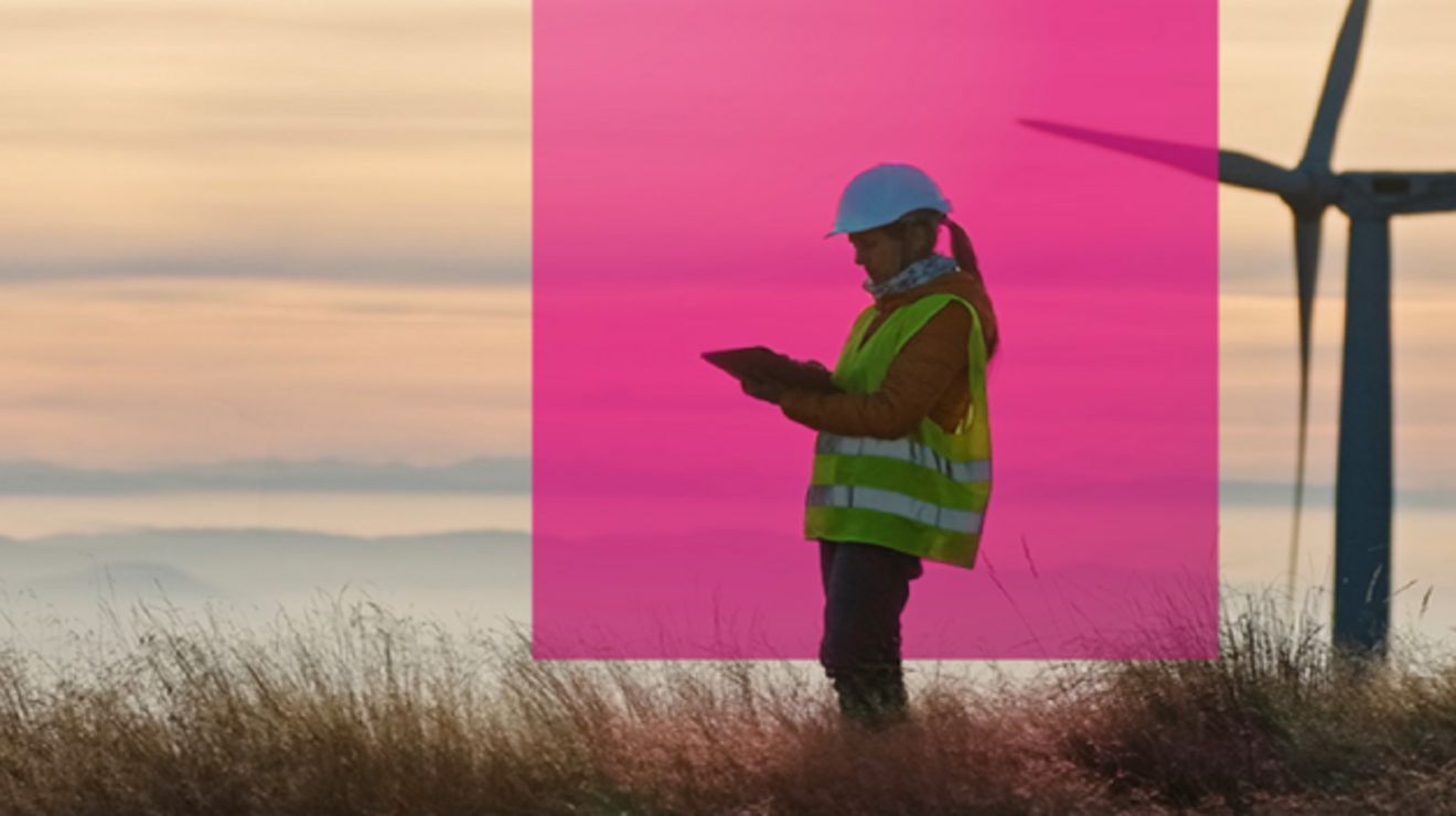 A wind energy engineer checks her tablet on a wind farm at dawn.