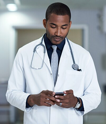 A doctor in a lab coat and stethoscope checks his smartphone in a hospital. 