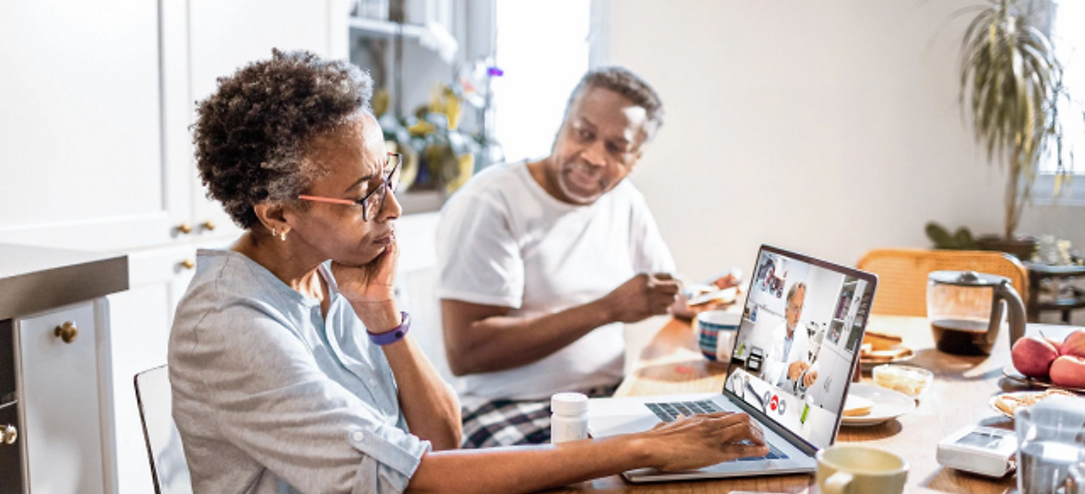 An older couple attends a telehealth appointment from their kitchen table.