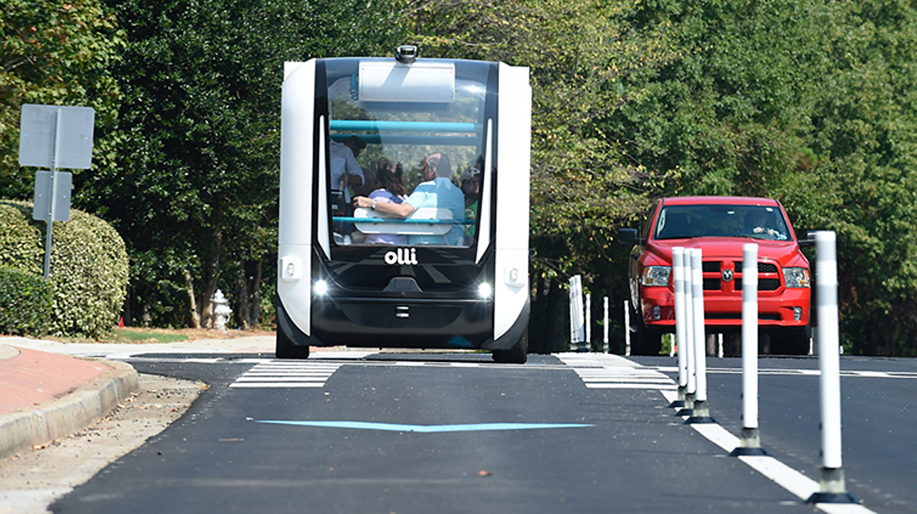 Two people embrace while riding down the street in a futuristic looking vehicle.