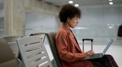 A professional traveling on business works on her laptop seated at an international airport gate.
