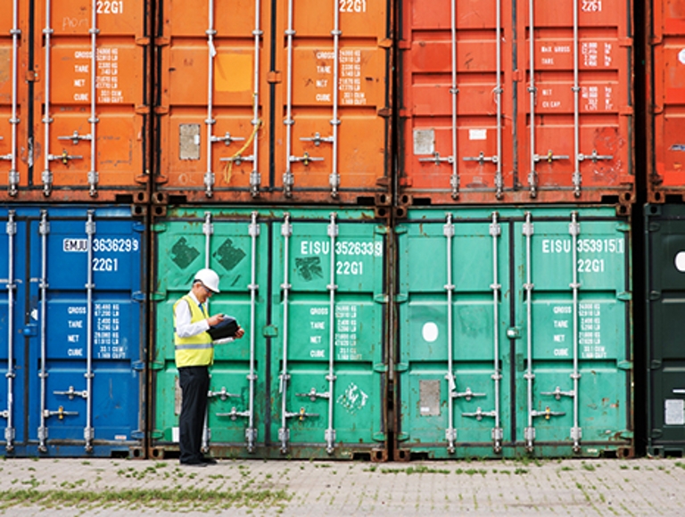 A worker inspects shipping containers with a connected mobile device.