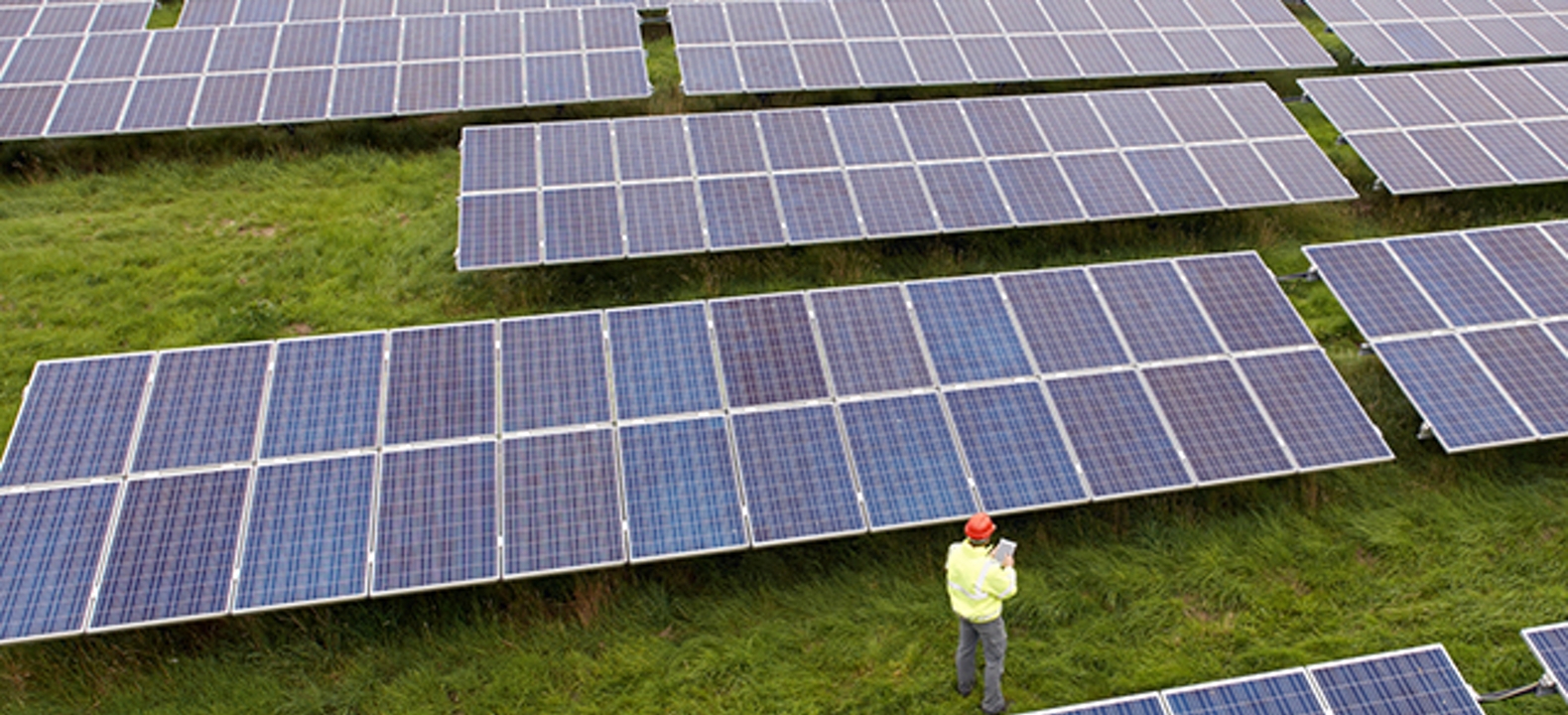 An overhead view of an engineer using a connected tablet to help inspect an array at a solar energy farm.
