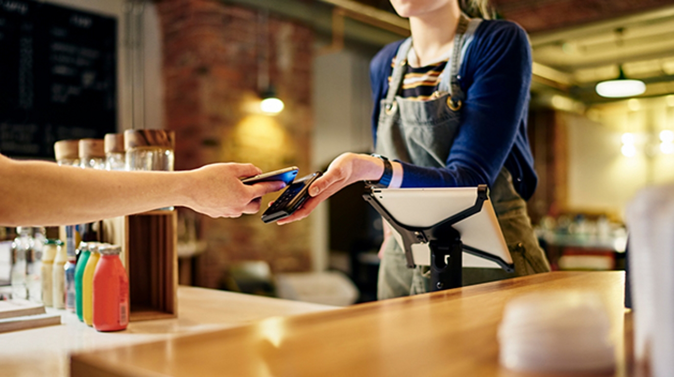 A barista at a coffee shop receives a payment on a card terminal connected to a secure network.