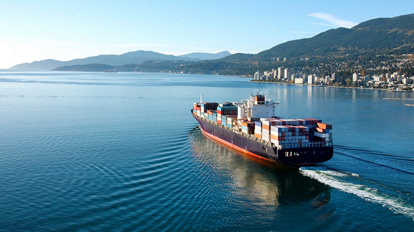A large ship with cargo containers approaches a city harbor.