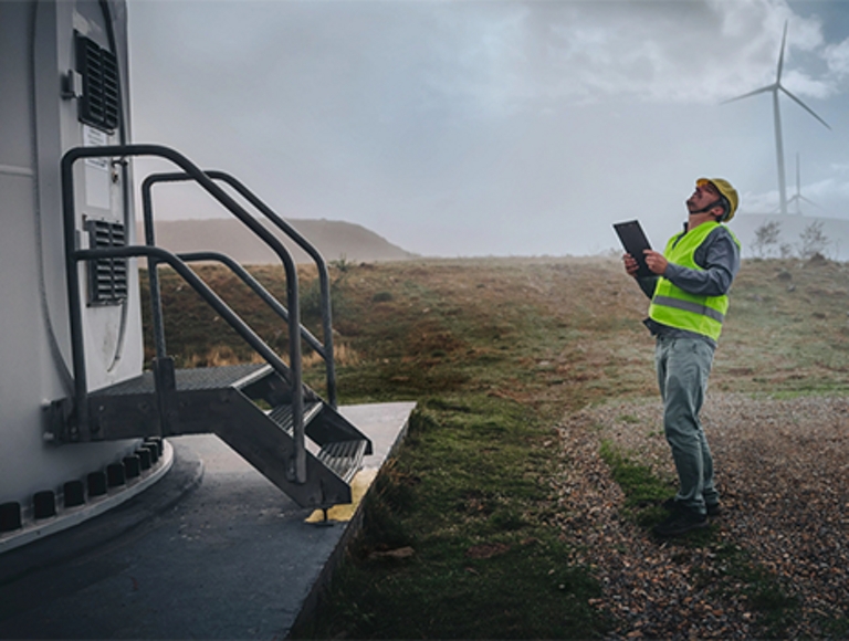 Worker on a wind farm looks up at equipment.