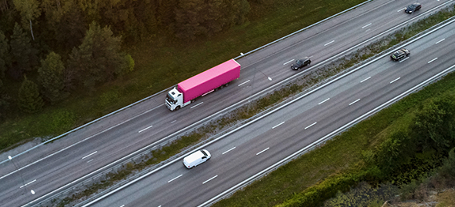 Overhead view of a highway with a white van and big rig with magenta and white colors 