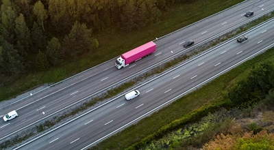 Overhead view of a highway with a big rig truck with magenta and white colors.