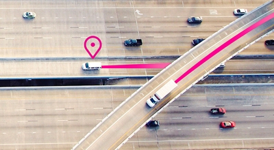 Two trucks travelling on a highway with a magenta location icon and paths indicating fleet tracking.