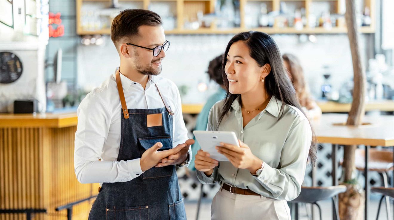 Small business owner and customer reviewing information on a tablet inside a café.