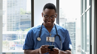 A smiling healthcare professional checks his smartphone.