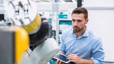 An engineer uses a tablet to operate machinery in a lab. 